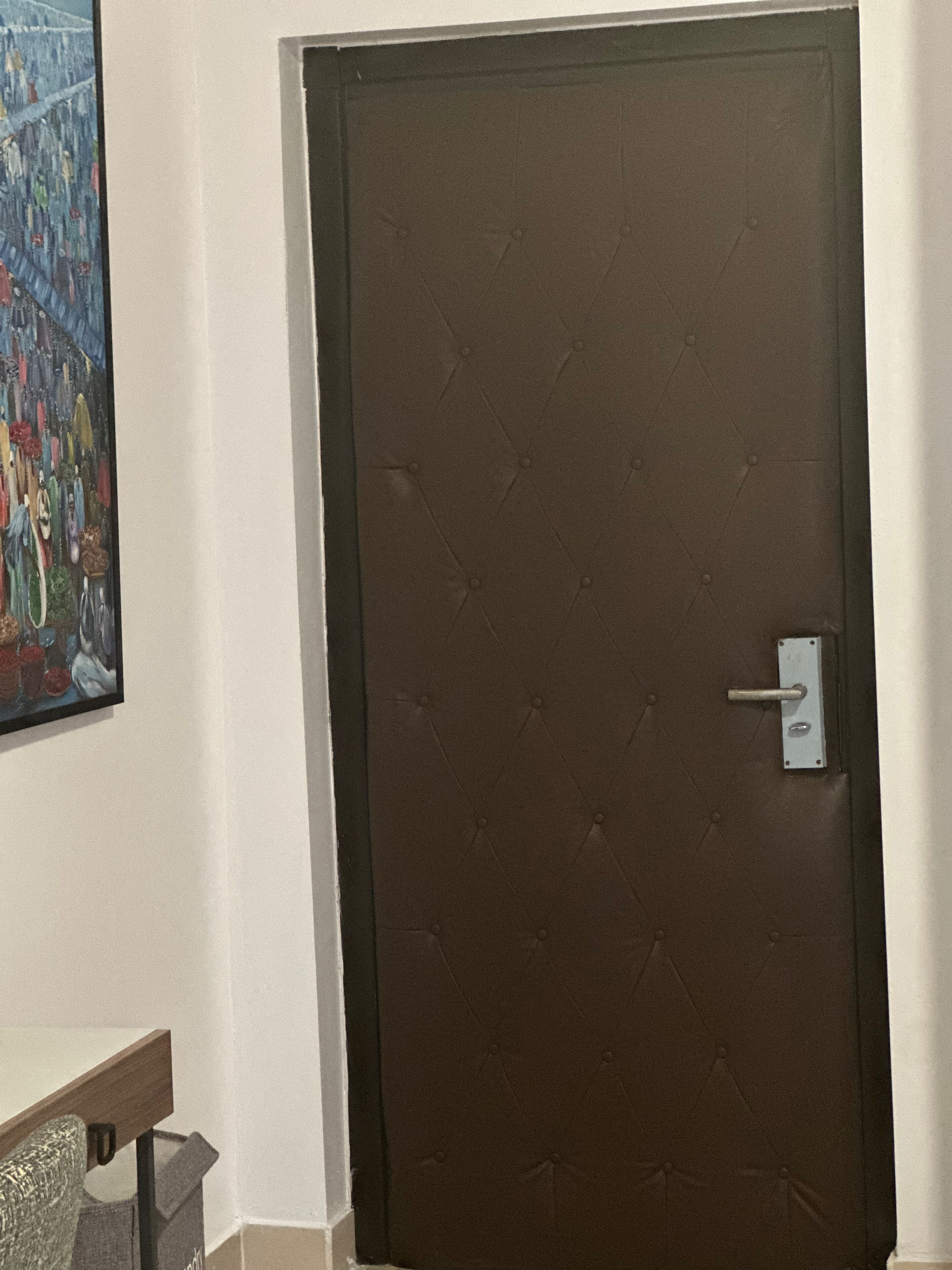 A closed brown door with a metal handle and a keyhole, a white wall, and a colorful painting on the left.