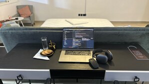 Una laptop sobre un escritorio con un vaso de agua, una taza y un plato de galletas.