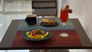 Una mesa con un plato de fruta, un vaso de bebida roja y una taza, sobre un mantel estampado.