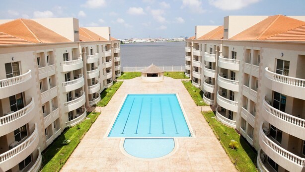Un hotel con una piscina central rodeada de numerosos balcones, vista al mar y cielo despejado.