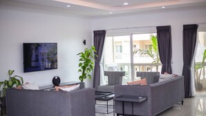 Un salón moderno con sofás grises, un televisor de pantalla plana y un ventanal con cortinas.
