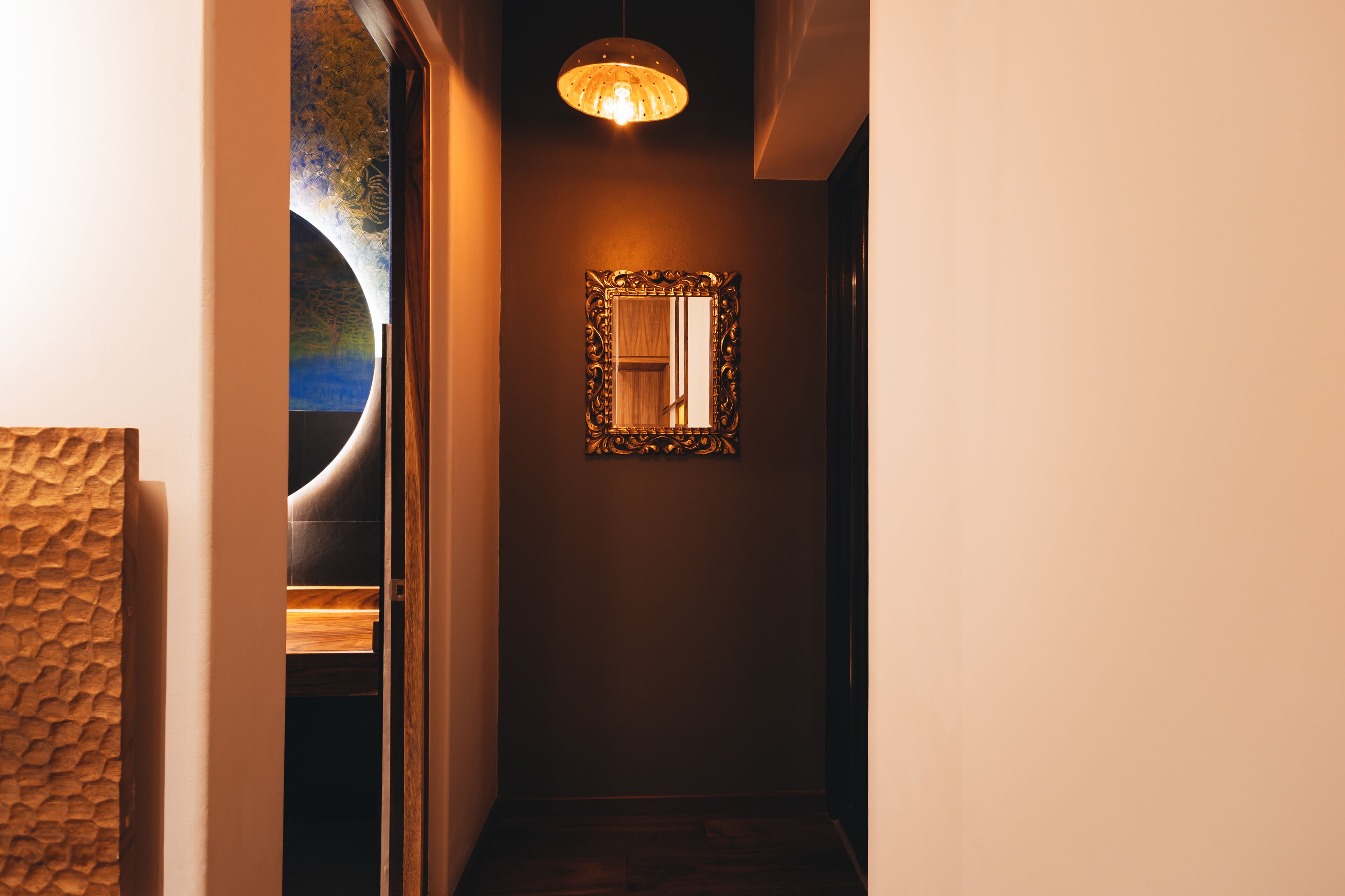 A hallway with a wooden door, a textured wall, a hanging light fixture, and a framed mirror on the wall.