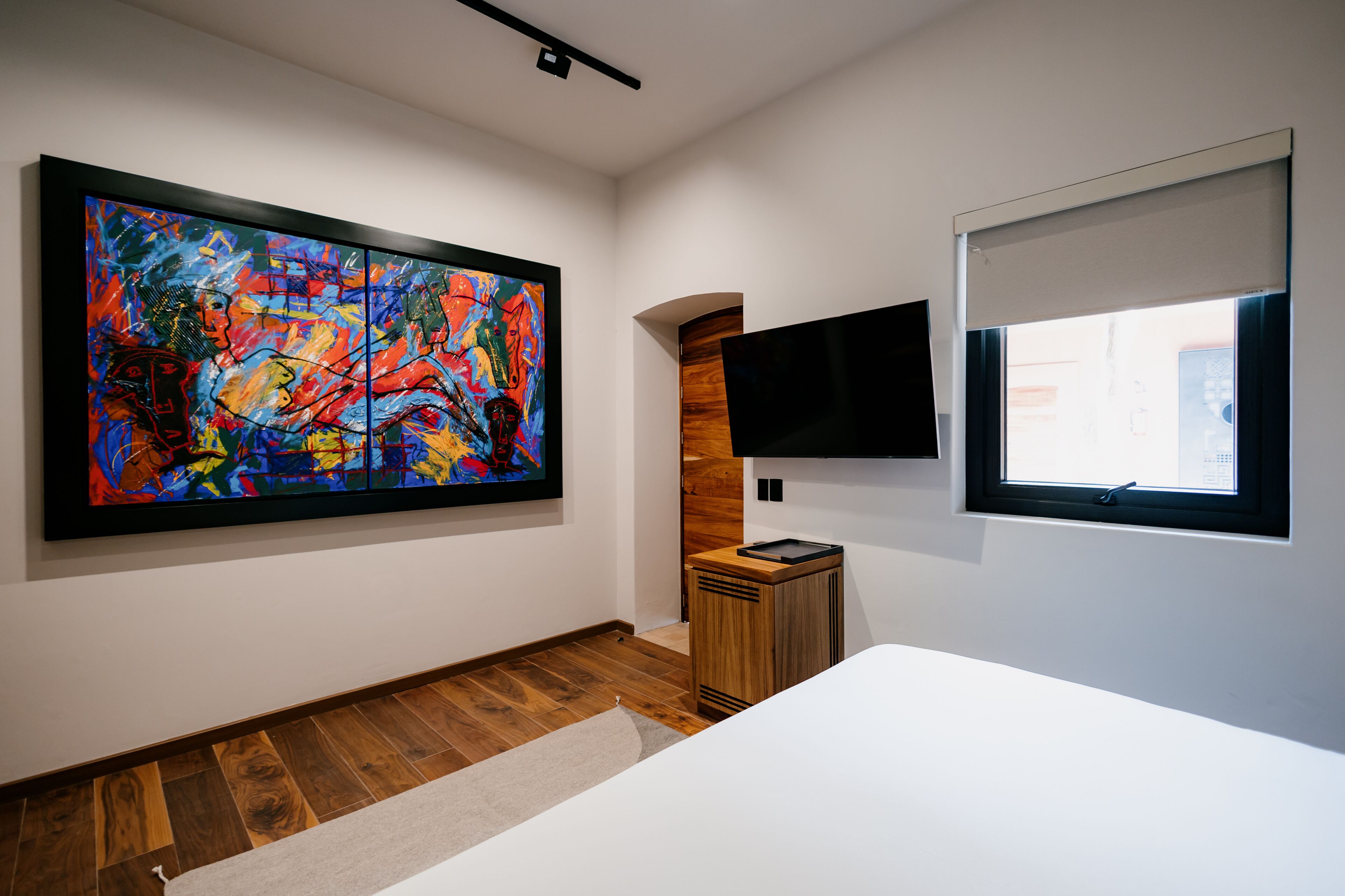 Una habitación de hotel moderna con un cuadro abstracto grande, un televisor de pantalla plana y un mueble de madera.