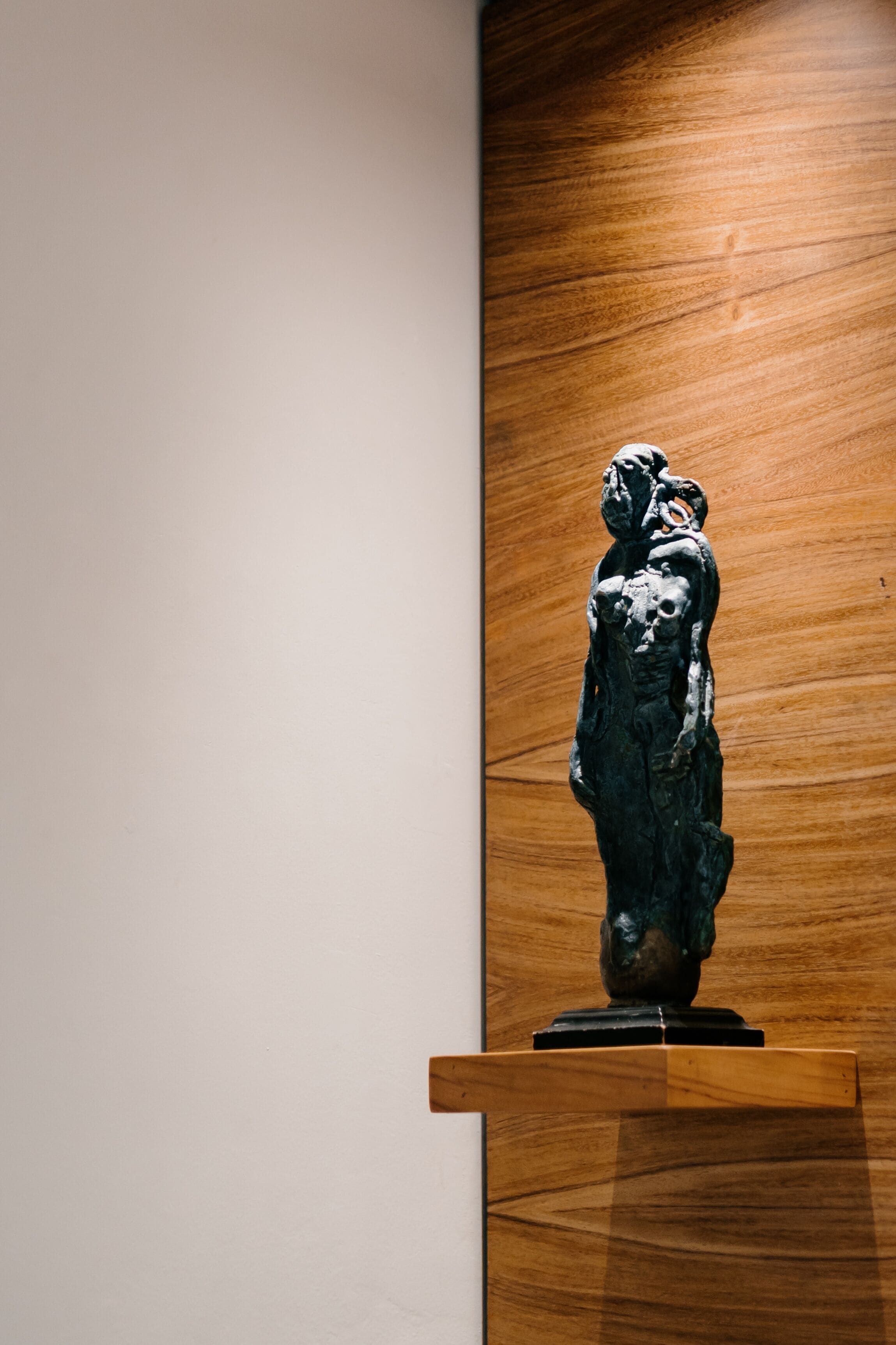 A sculpture on a wooden pedestal against a plain wall.