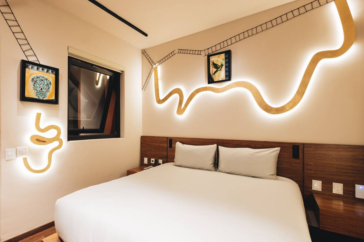 A modern hotel room with a large bed, a window, and wall art.