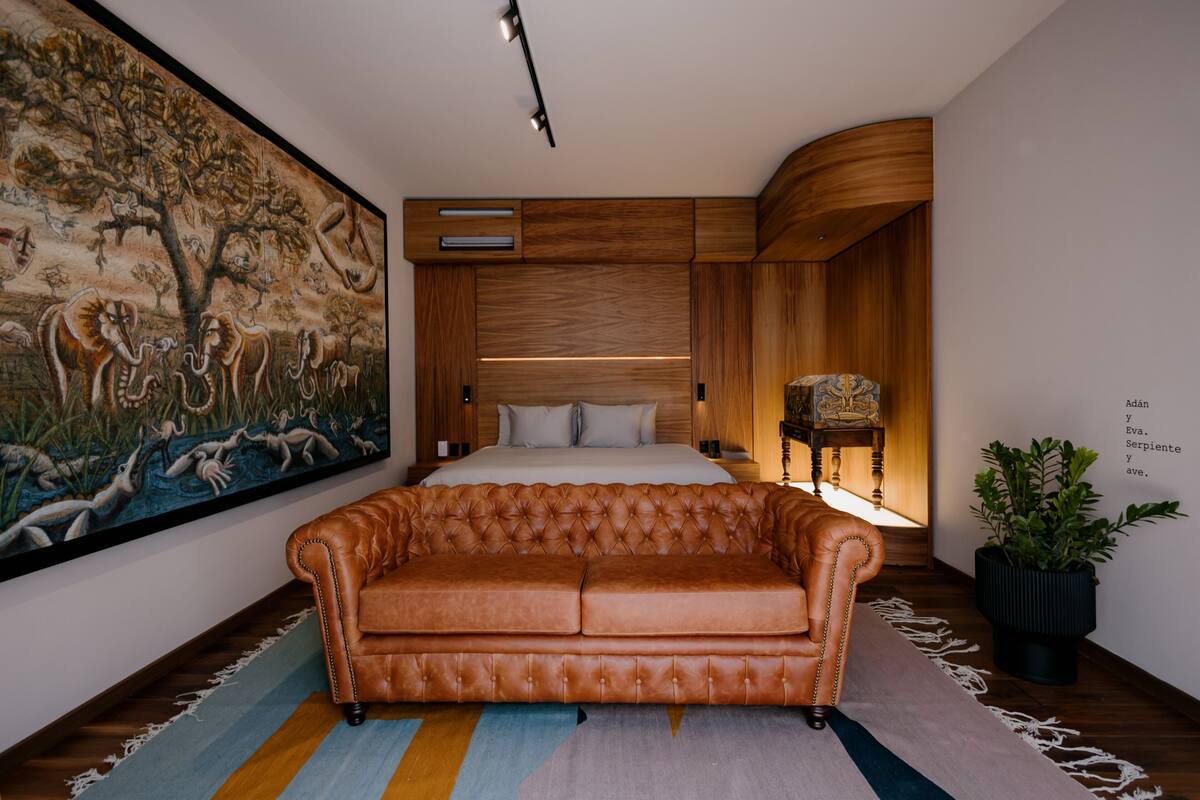 A bedroom with a large bed, a leather sofa, a wooden headboard, and a large painting on the wall.