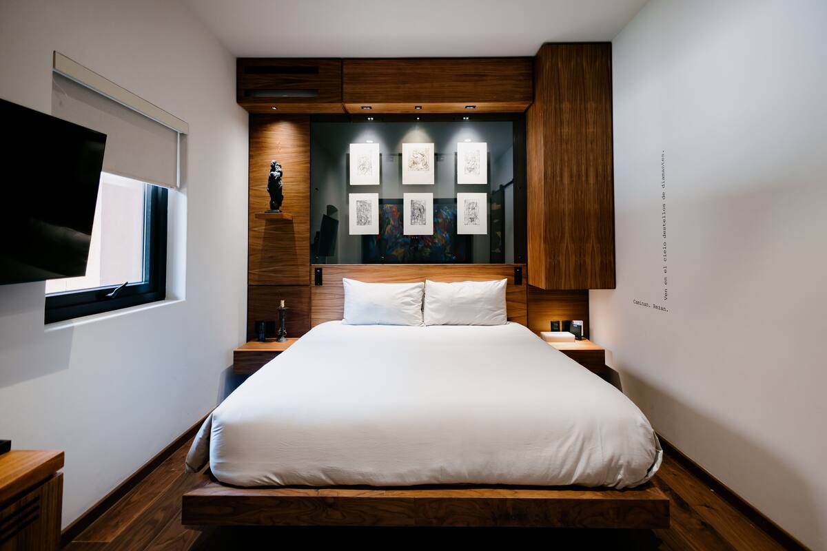 A modern bedroom with a large bed, wooden headboard, and artwork on the wall.