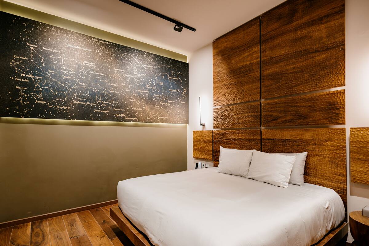 A modern hotel room with a large bed, a cityscape wall art, and a textured wooden headboard.