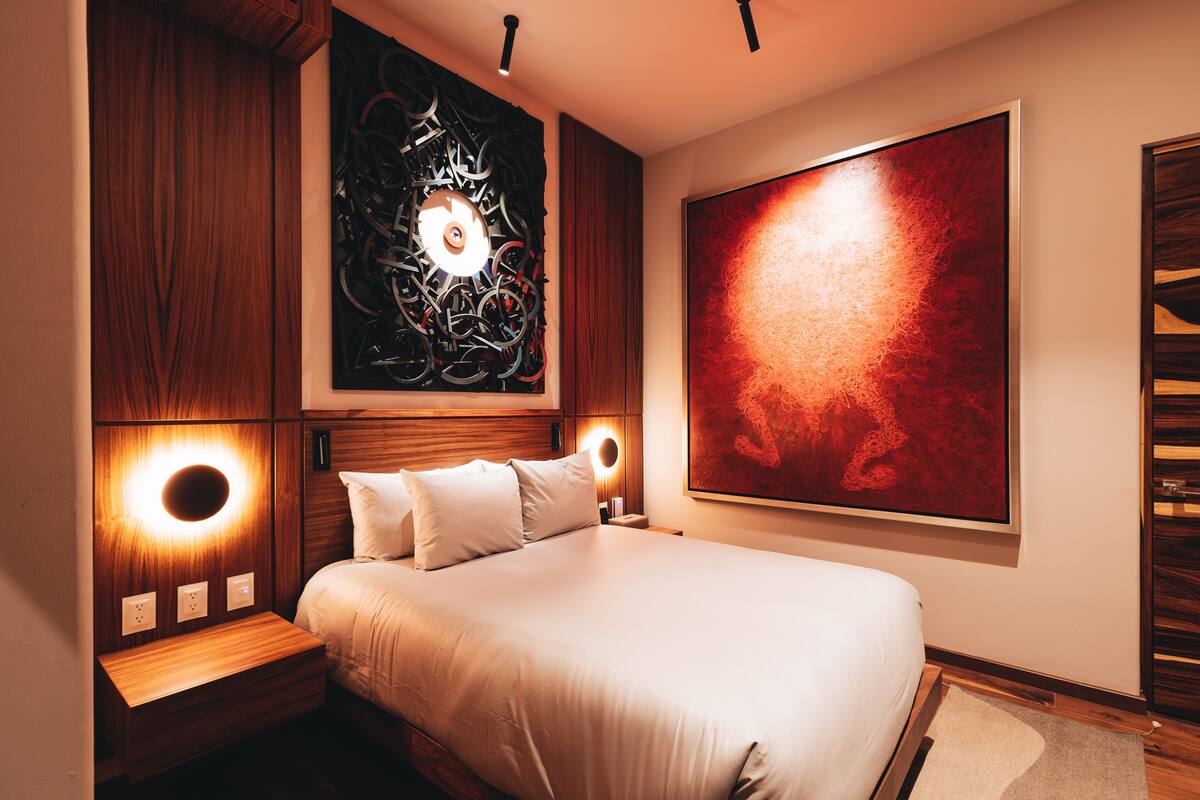 A modern bedroom with a large bed, wooden headboard, and two wall-mounted reading lights.