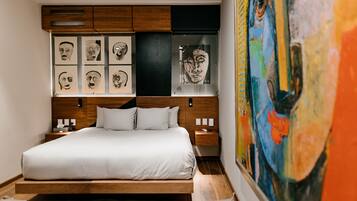 A modern bedroom with a wooden bed frame, white bedding, and a large abstract painting on the wall.