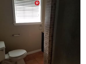 Ein kleines Badezimmer mit Toilette, einem Fenster mit Jalousien und einer Duschvorhang.