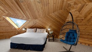 A cozy attic bedroom with a large bed, a hanging chair, and a skylight. - The Turtle Shell Dome (Berthoud)