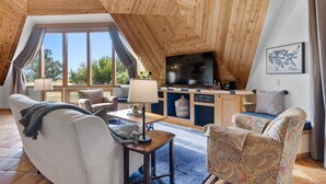 A cozy, wooden-paneled living room with a large TV, comfortable seating, and a view of the outdoors. - The Turtle Shell Dome (Berthoud)