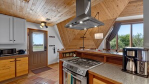 A kitchen with wooden cabinets, a stove, a coffee maker, and a large window. - The Turtle Shell Dome (Berthoud)