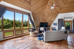A spacious living area with a large window, a ceiling fan, and a TV.