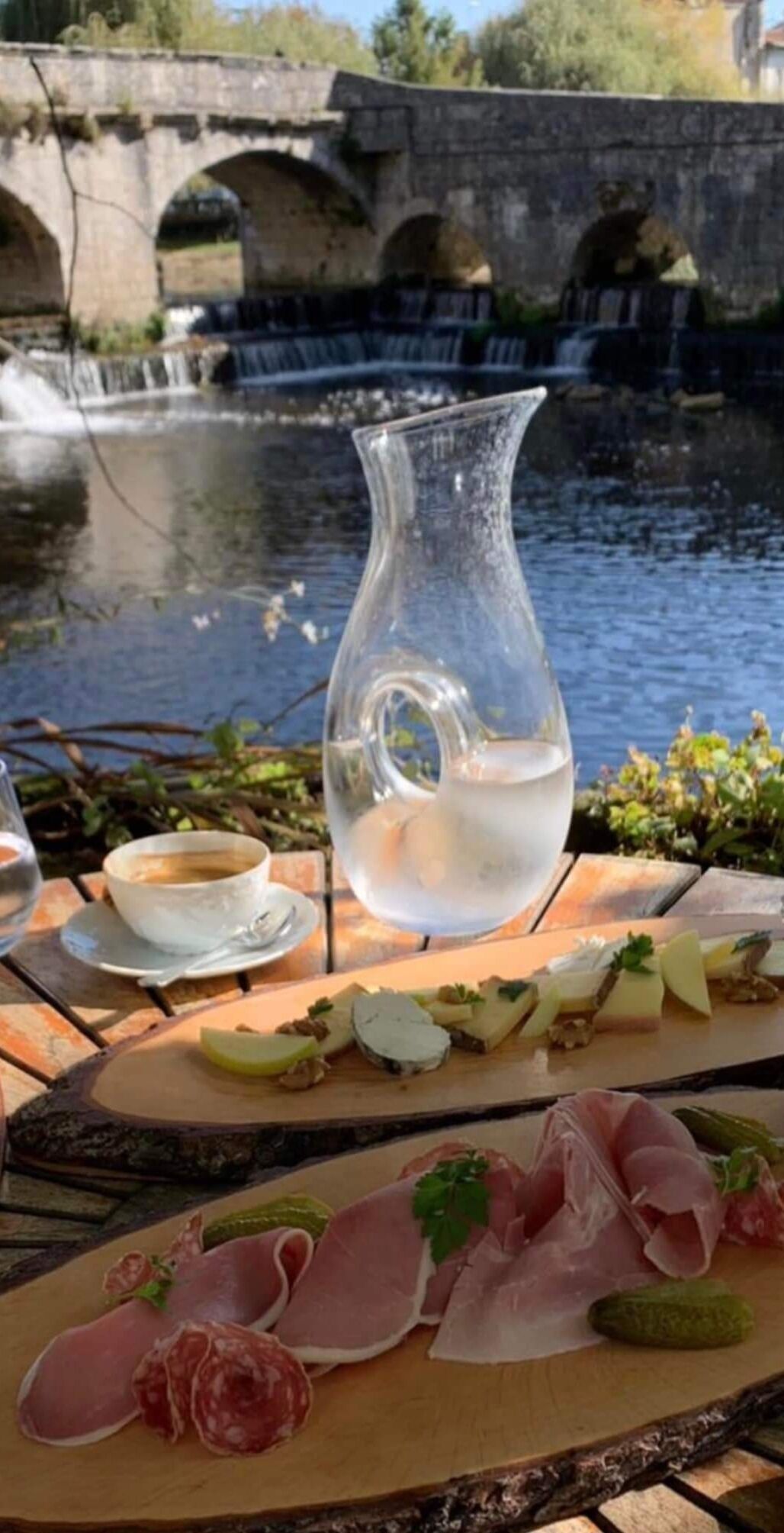Ein Tisch mit einer Wasserkanne, einer Tasse Kaffee und verschiedenen Speisen, darunter Fleisch und Käse.