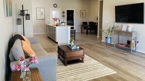 A modern living room with a grey sofa, wooden coffee table, and a dining area with a TV and console table. - Cozy home # Safe Neighborhood & Pet Friendly (Lubbock)