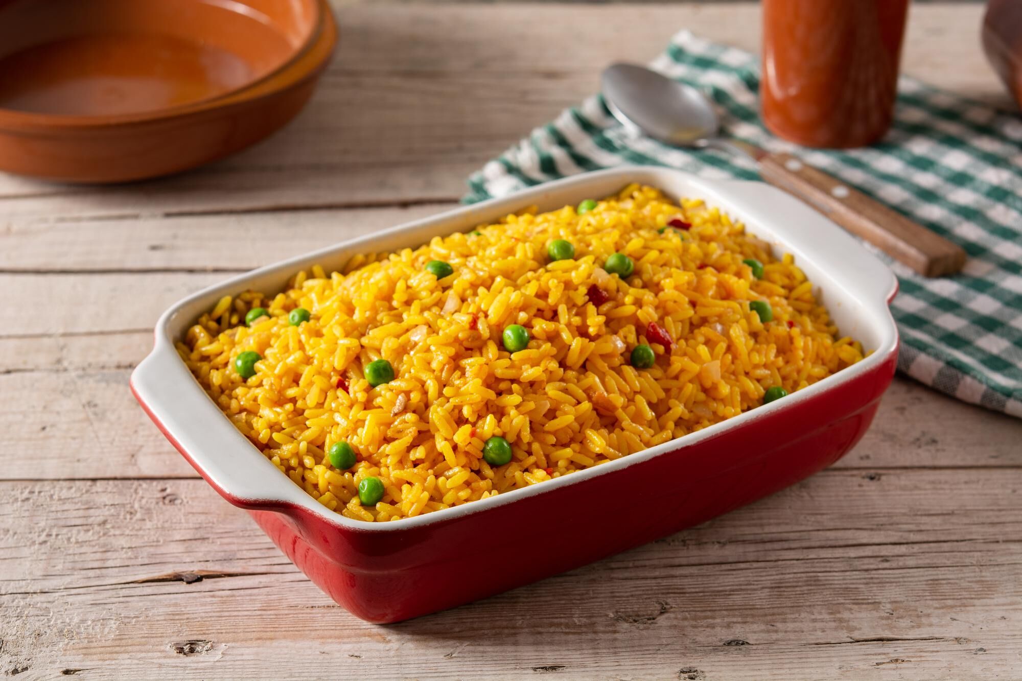A red baking dish filled with yellow rice and green peas on a wooden table.