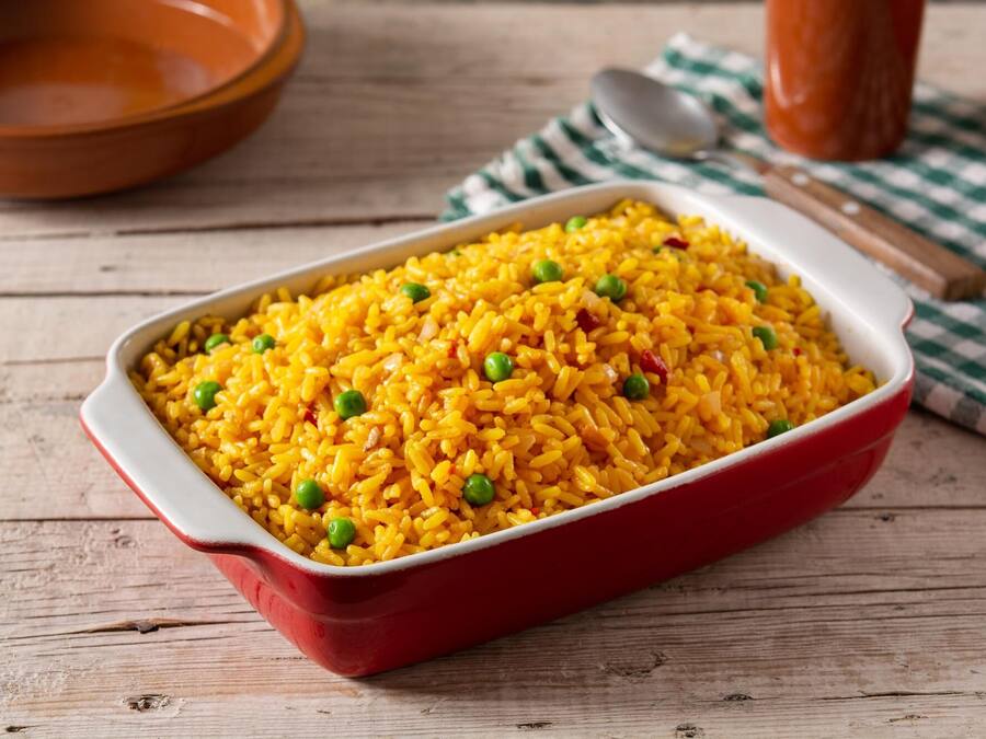 A red baking dish filled with yellow rice and green peas on a wooden table.