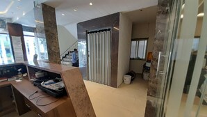 A modern hotel lobby with a reception desk, a staircase, and a large window.