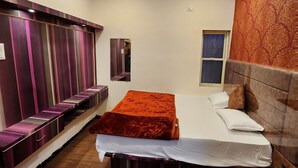 A hotel room with a bed, a seating area, a wardrobe, and a ceiling fan.