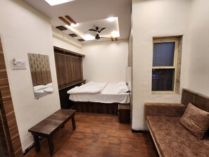 Quarto compacto com cama, um banquinho, um sofá, ventilador de teto e janela.