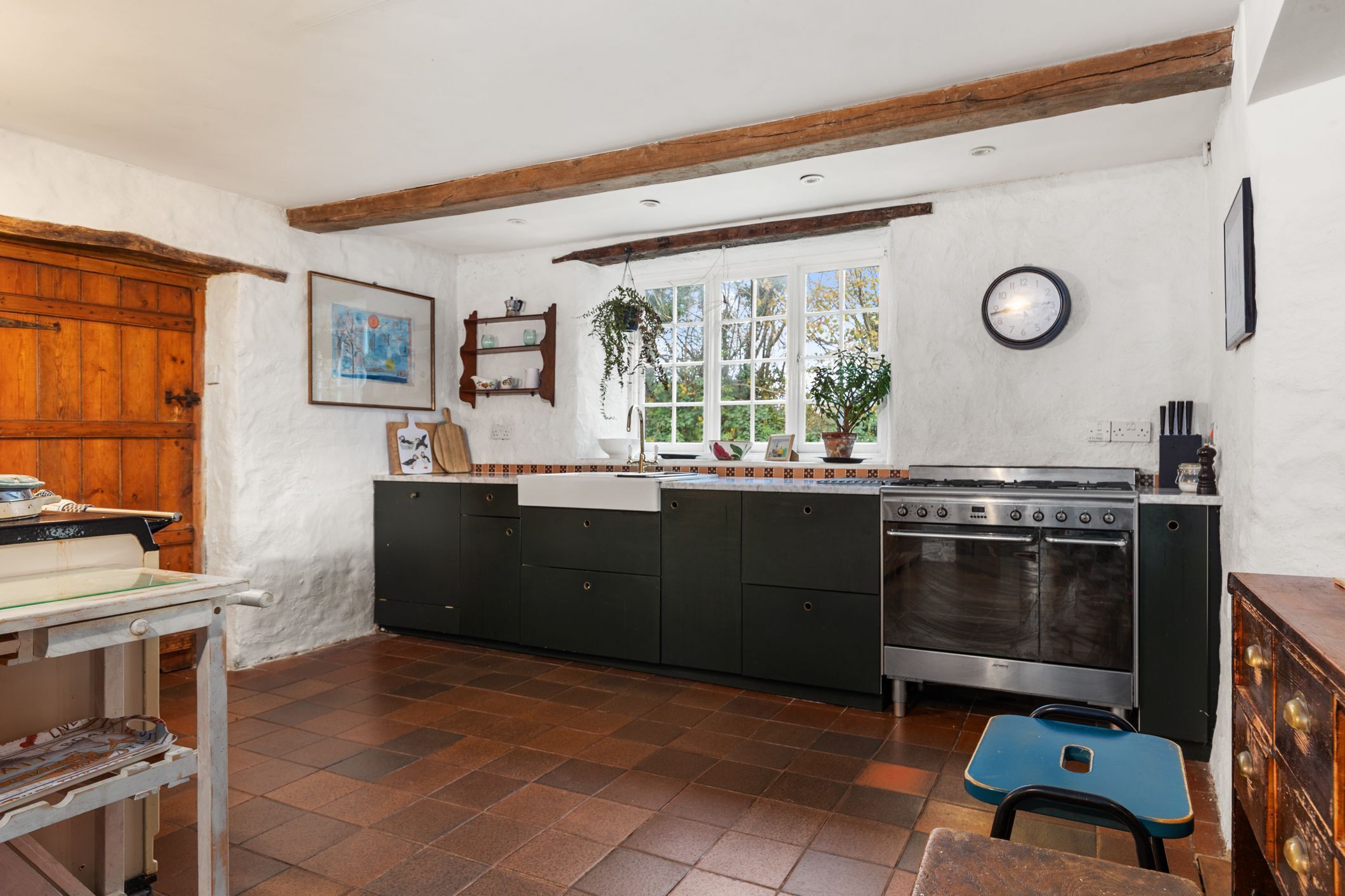 A kitchen with a large stove, wooden cabinets, a window with a view, and a clock on the wall.