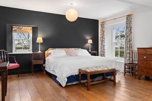 Une chambre à coucher avec un grand lit, deux lampes de chevet, un banc en bois, une commode et une fenêtre avec des rideaux.