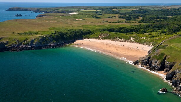 Luchtbeeld van een kustgebied met een strand, kliffen en een heldere lucht.