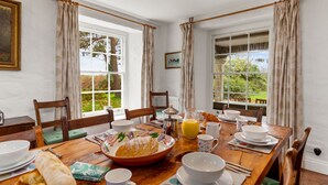 Een eetkamer met een houten tafel gedekt voor het ontbijt, inclusief croissants, koffie en sap.