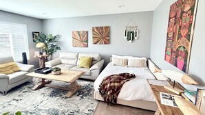 A living room with a sofa, a coffee table, a bed, and a large painting on the wall. - The Ultimate Gateway, near Monterey, Carmel, Pebble Beach, Big Sur- STR25-000022 (Marina)