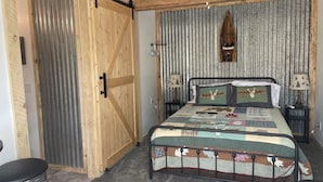A bedroom with a bed, two bedside tables, a ceiling fan, a wooden door, and a metal stool.