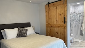 A bedroom with a large bed, a wooden wardrobe, and a bathroom with a shower curtain.
