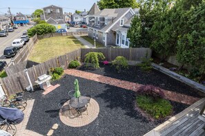 Een achtertuin met terras, barbecue en houten omheining.