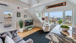 Een ruime woonkamer met een groot raam, een flatscreen-tv, een comfortabele bank en een eethoek met een marmeren tafel.