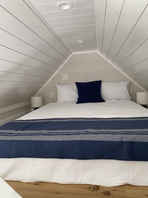 Een slaapkamer met een schuine kap, een bed met wit en marineblauwe beddengoed, en twee bedlampjes.
