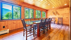 A wooden interior with a dining table and chairs, large windows with a forest view, and a ceiling with wooden beams. - Large, Luxury, Views, Near Whiteface, Lake Placid (Wilmington)