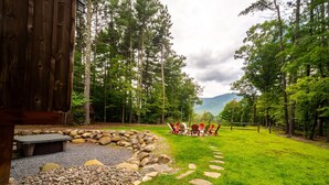 A wooden cabin with a stone fire pit and red Adirondack chairs facing a grassy area with a stone path. - Large, Luxury, Views, Near Whiteface, Lake Placid (Wilmington)