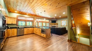 A spacious kitchen with wooden cabinets, a central island, and a stone fireplace. - Large, Luxury, Views, Near Whiteface, Lake Placid (Wilmington)