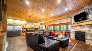 A spacious living area with a large leather sofa, a stone fireplace, and a kitchen with wooden cabinets and a stainless steel refrigerator. - Large, Luxury, Views, Near Whiteface, Lake Placid (Wilmington)