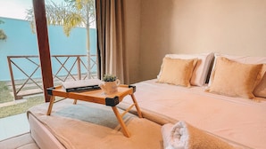 Una camera da letto con un letto grande, un comodino in legno e vista su palme attraverso una finestra.