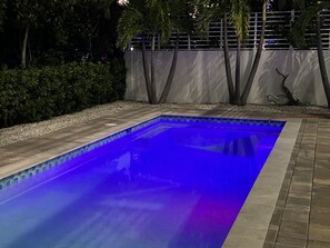 A rectangular swimming pool with a tiled edge, surrounded by a pebble-lined walkway and a low hedge.