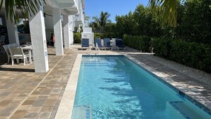 A rectangular pool with clear blue water, surrounded by a tiled deck and lounge chairs.
