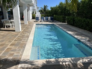 A rectangular pool with clear blue water, surrounded by a tiled deck and lounge chairs.