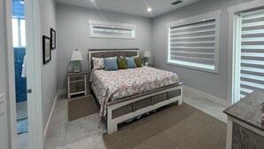 A bedroom with a bed, bedside tables, a window with blinds, and a ceiling vent.
