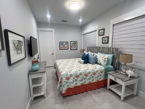 A bedroom with a bed, bedside tables, a TV, and framed pictures on the wall.