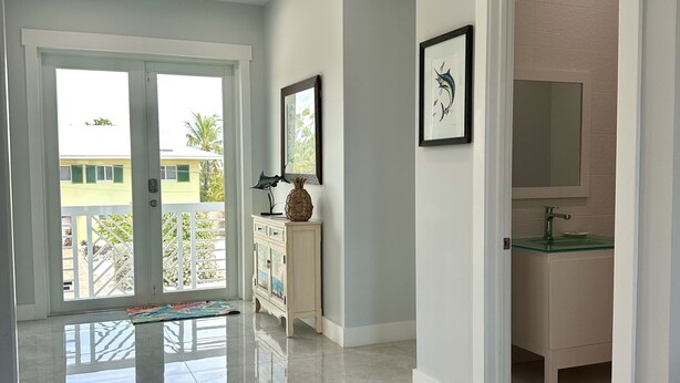 A spacious hallway with a polished floor, a white cabinet with decorative items, a framed picture, and a glass-top vanity with a red rug.
