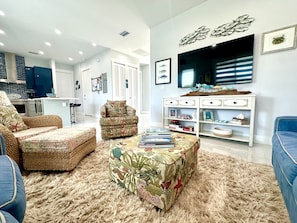 A living room with a sofa, armchair, and a coffee table. There is a bookshelf with decorative items and a flat-screen TV mounted on the wall. - Coastline Marine Extremes ChillN (Marathon)