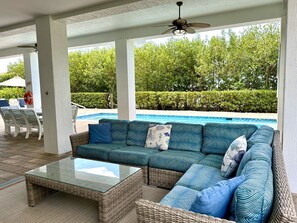 A covered outdoor seating area with a pool, wicker furniture, and a ceiling fan.