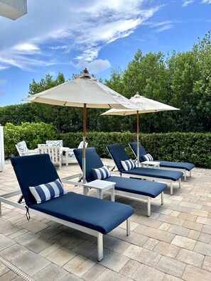 A patio area with lounge chairs and umbrellas, surrounded by greenery.
